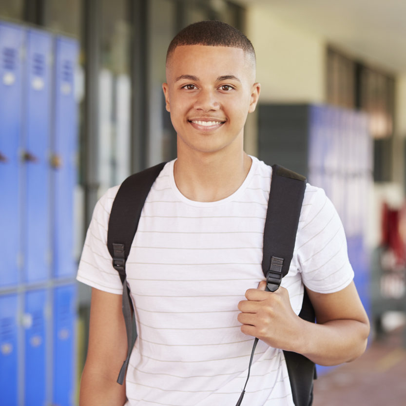 Happy mixed race teenage boy smiling in high school corridor